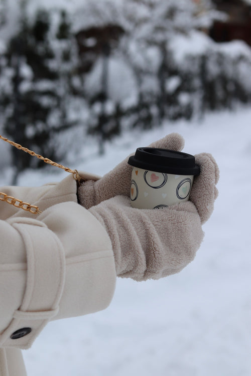 Gloved hands holding a warm drink in the snow